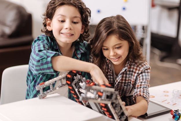 Acessando tecnologias modernas. Divertiram crianças curiosas e positivas sentadas na sala de aula de ciências e usando gadgets e dispositivos enquanto expressavam alegria