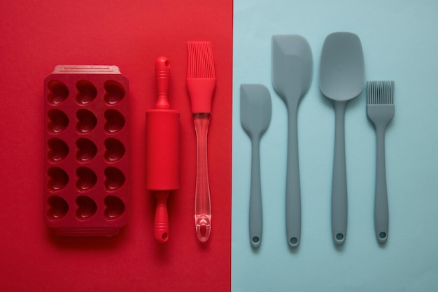 Acessórios culinários de silicone, espátulas, pincéis moldam o rolo sobre fundo culinário vermelho e azul