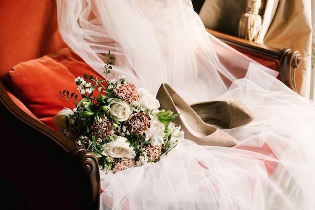 Acessórios de casamento do véu de sapatos de buquê de noiva em uma cadeira vermelha