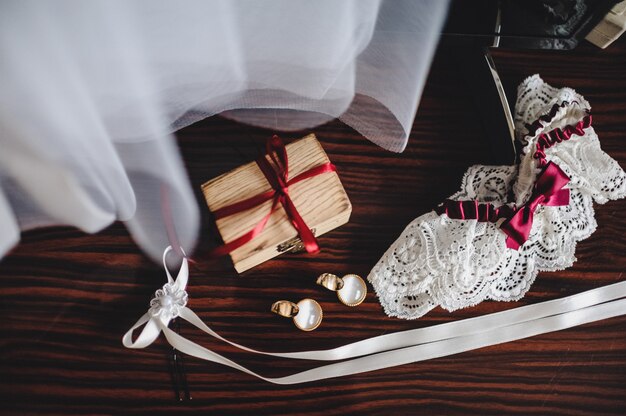 Acessórios de casamento, vestido, brincos, caixa e liga, deitado sobre uma mesa marrom
