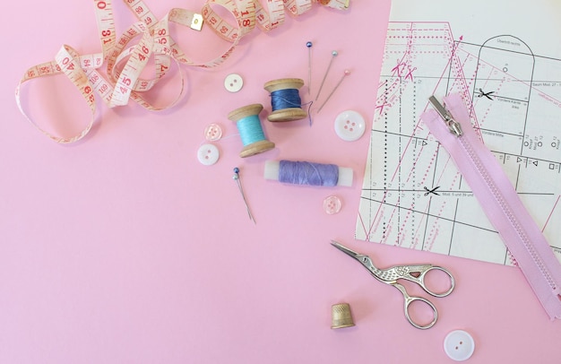 Acessórios de costura e tecido em um fundo rosa Linhas de costura agulhas pinos botões de tecido e costura centímetro vista superior flatlay