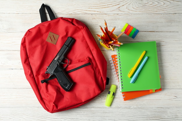 Acessórios de escola e arma na mesa de madeira branca. Violência escolar