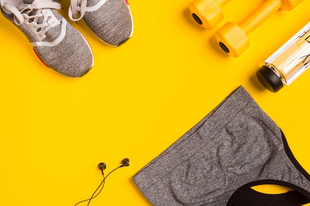 Acessórios de fitness em uma garrafa de tênis de fundo amarelo de fones de ouvido de água e top esporte