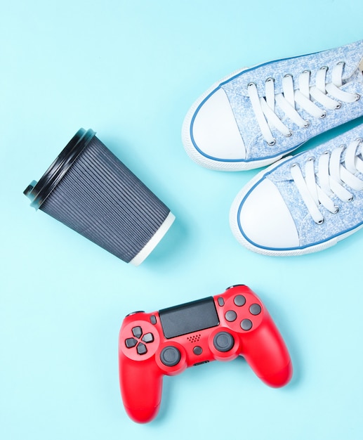 Acessórios de hipster juventude estilo plana leigos sobre fundo azul pastel. Gamepad vermelho, tênis, copo de café de papel