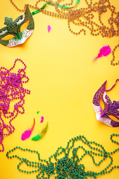 Foto acessórios de mardi gras planas leigos em fundo amarelo brilhante, vista superior, espaço de cópia. moldura com miçangas tradicionais de mardi gras, máscaras, plumas planas. conceito de feriado de carnaval acima da cabeça