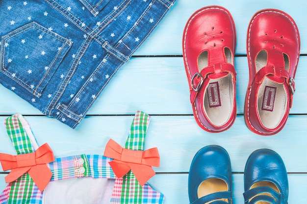 Acessórios de menina. vestido colorido, sapatos e jeans na superfície de madeira pastel azul.