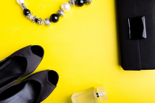 Acessórios de moda senhora conjunto preto e amarelo sapatos pretos mínimos, pulseira, perfume e bolsa na superfície amarela