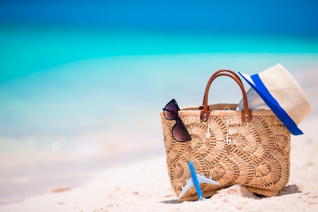 Acessórios de praia - bolsa de palha, fones de ouvido, avião de brinquedo e óculos de sol na praia