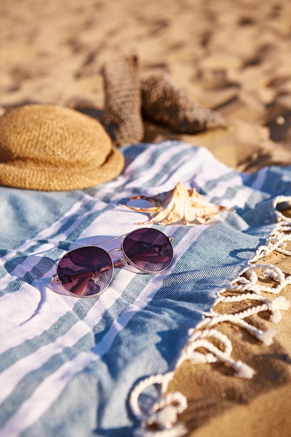 Acessórios de praia de verão - óculos de sol, chapéu, concha no cobertor e areia