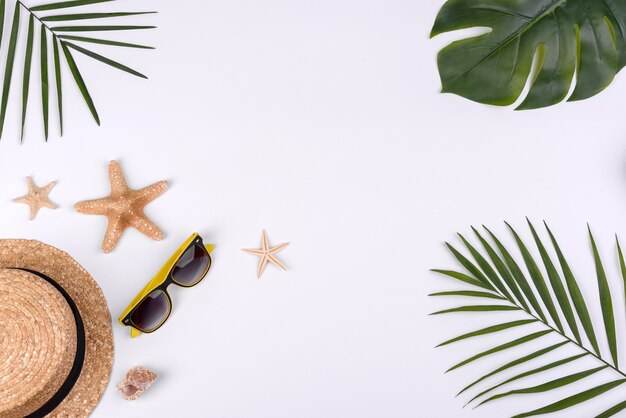 Acessórios de praia: óculos e chapéu com conchas e estrelas do mar em fundo branco. Fundo de verão