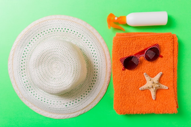 Acessórios lisos da praia do verão. Creme de frasco de protetor solar, toalha e conchas em fundo colorido. Conceito de viagens de férias com espaço de cópia.