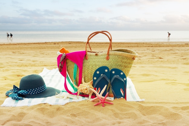 Acessórios para banho de sol em bolsa de palha na praia à beira-mar