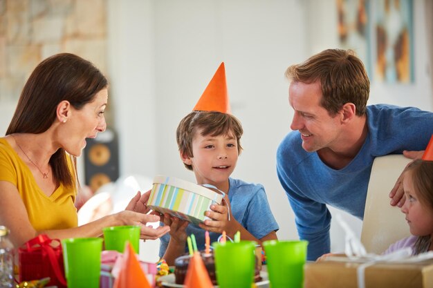 Acho que sei o que é isso Foto de um garotinho abrindo seus presentes de aniversário cercado por sua família