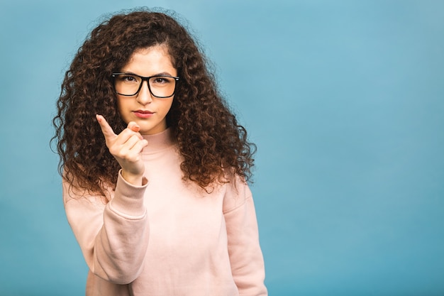 Achtung, hör mir zu! Schließen Sie herauf Porträt der jungen lockigen Frau, die ihren Finger lokalisiert über blauem Hintergrund wedelt.