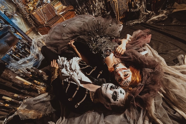 Acima, casal de Halloween deitado no chão do estúdio com um interior místico. Homem e mulher maquiados
