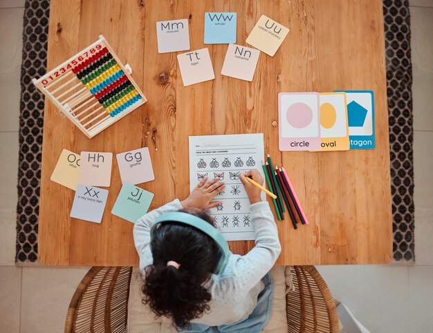 Foto acima, criança e menina escrevendo na mesa para lição de casa ou aprendizado remoto em casa para desenvolvimento, crescimento e educação criança trabalhando e estudando para matemática escolar e escrevendo em papel na sala de estar