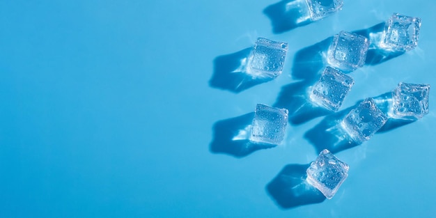 Acima da cabeça, feche a foto macro de cubos de gelo e gotas de água sobre fundo azul