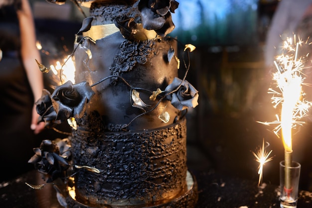 Acima de velas acesas, fogos de artifício ficam em um bolo e uma mão paira sobre ele