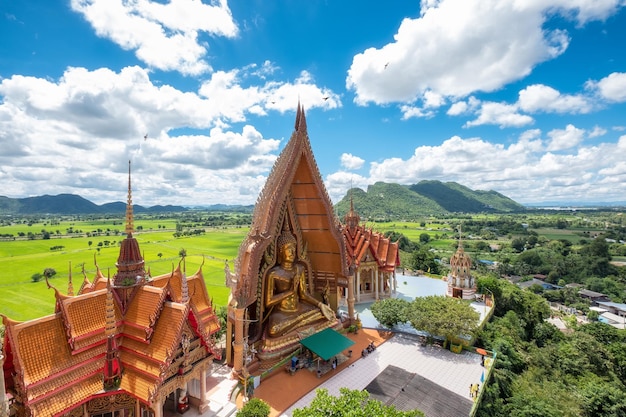 Acima vista da igreja dourada com grande estátua de Buda e campo de arroz no templo Wat Tham Sua