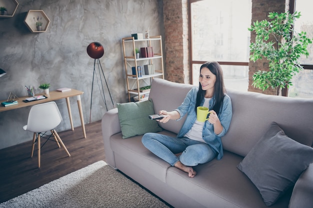 Acima, vista de alto ângulo, foto em tamanho grande de menina alegre positiva covid19 tempo livre quarentena relaxar assistir tv mudar de canal segure café bebida caneca sente divã pernas cruzadas em casa