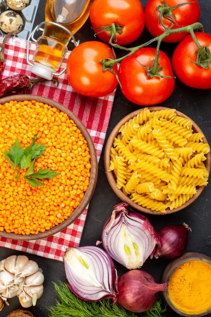 Acima vista de lentilhas vermelhas em uma tigela marrom no tomate toalha com haste caída garrafa de óleo sal pacote verde pimenta seca