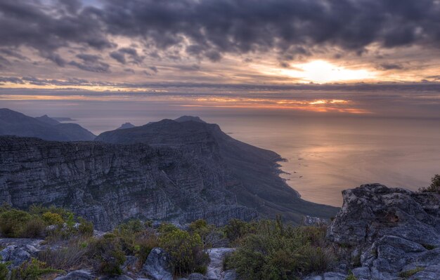 Acima vista de um litoral de montanha ao pôr do sol na África do Sul Paisagem cênica de nuvens escuras sobre um oceano calmo e pacífico perto da Cidade do Cabo com o sol atrás de nuvens cinzentas no céu e espaço de cópia
