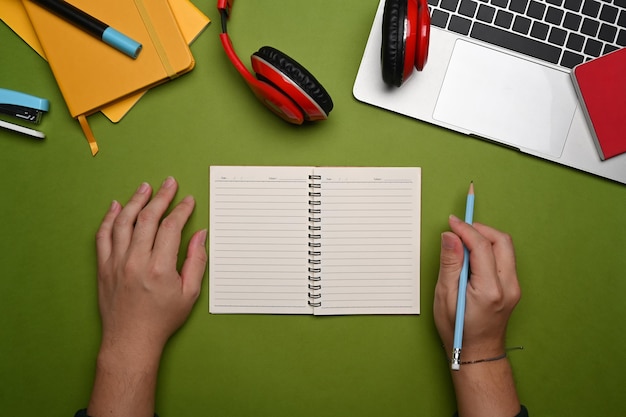 Acima vista jovem segurando o lápis e escrevendo no caderno.