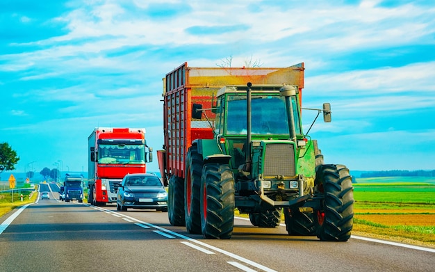 Ackerschlepper mit Anhänger auf der Straße. Ackerwagen bei der Arbeit auf der Auffahrt. Europäischer Verkehr. Transport auf dem Land auf der Autobahn.