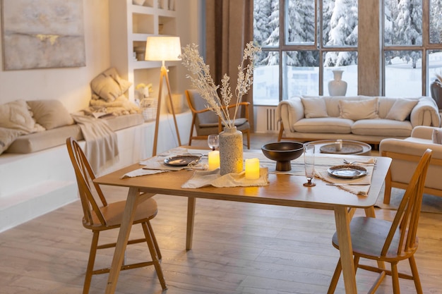 Acogedor y cálido interior de un elegante chalet de campo con una enorme ventana panorámica con vistas al bosque de invierno, decoración de madera de planta abierta, colores cálidos y un hogar familiar