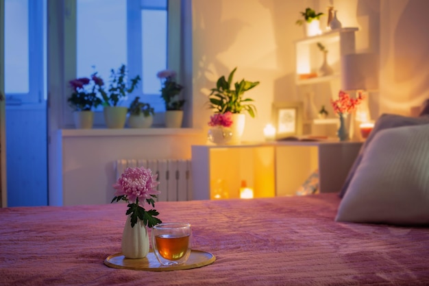 Acogedor dormitorio por la noche con flores y té.