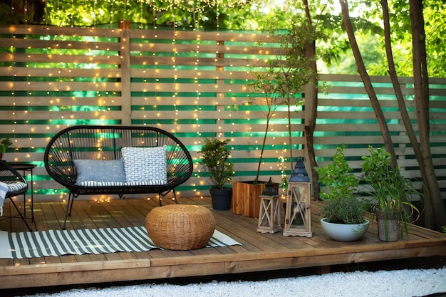 Acogedor espacio en patio con plantas, pared de madera y mesa, cómodo sofá y linternas.