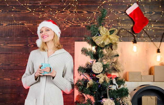 Acogedor hogar Mujer celebra la Navidad en casa Chica con gorro de Papá Noel lista para recibir el año nuevo Mujer con taza celebrando las vacaciones de invierno Navidad Concepto de Nochebuena Receta de chocolate caliente Beber café