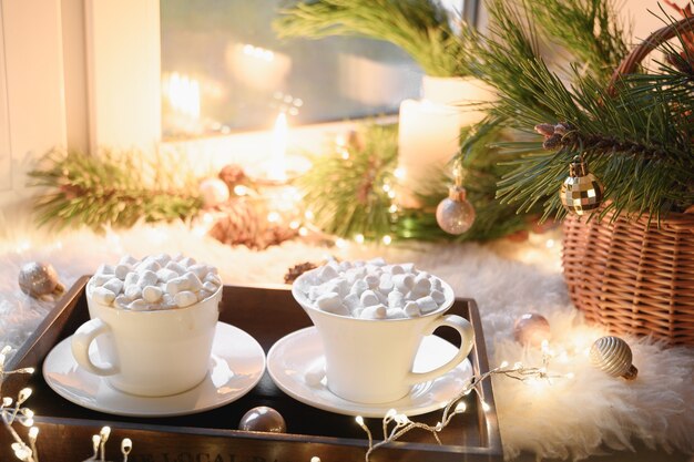 Acogedor horario de invierno con velas de malvavisco de café navideño y guirnaldas en el alféizar de la ventana