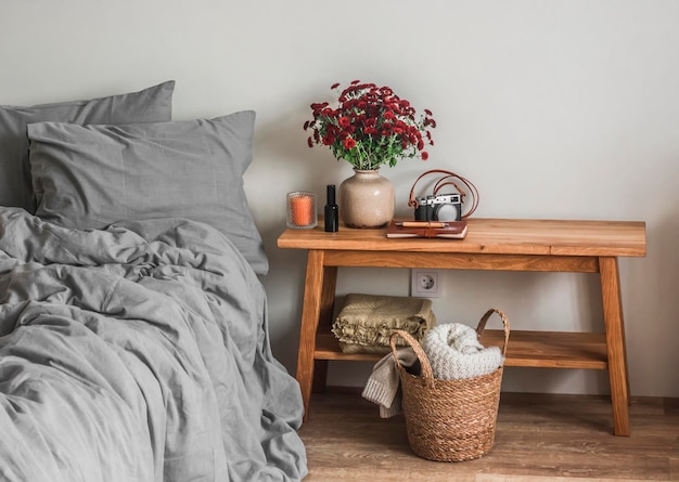 Acogedor interior de dormitorio una cama con sábanas de lino un ramo de crisantemos rojos en un banco de madera una cesta con mantas