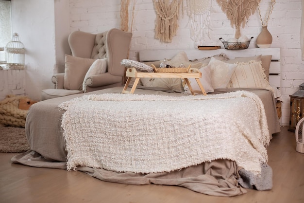 Acogedor interior escandinavo de dormitorio con sillón y cama con una mesita en la cama y almohadas