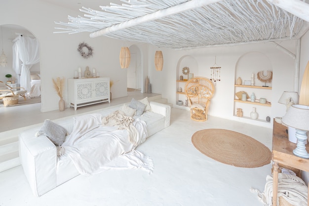 Acogedor interior de un luminoso apartamento de estilo balinés con paredes blancas, silla de bambú, gran sofá blanco y decoraciones