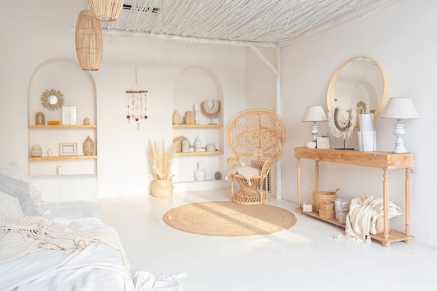 Acogedor interior de un luminoso apartamento de estilo balinés con paredes blancas, silla de bambú, gran sofá blanco y decoraciones