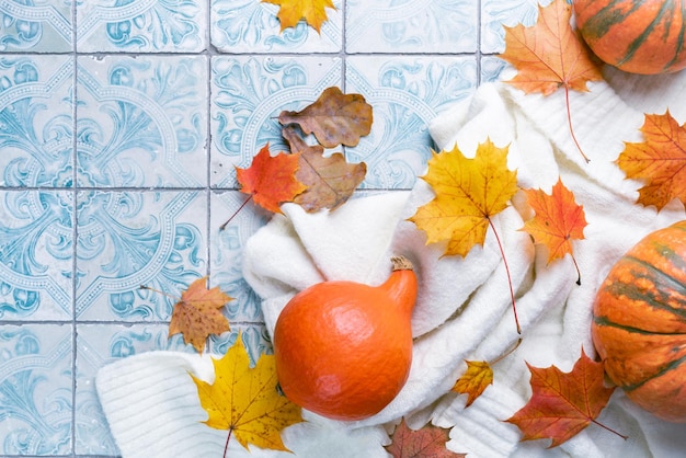 Acogedor piso de otoño con calabazas suéter de lana de punto y velas de hojas de otoño en el fondo del azulejo