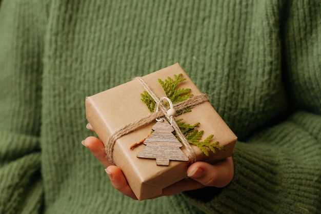 Acogedor regalo de Navidad en la mano de la mujer cerca de una pequeña caja de regalo dof decorada con decoración ecológica