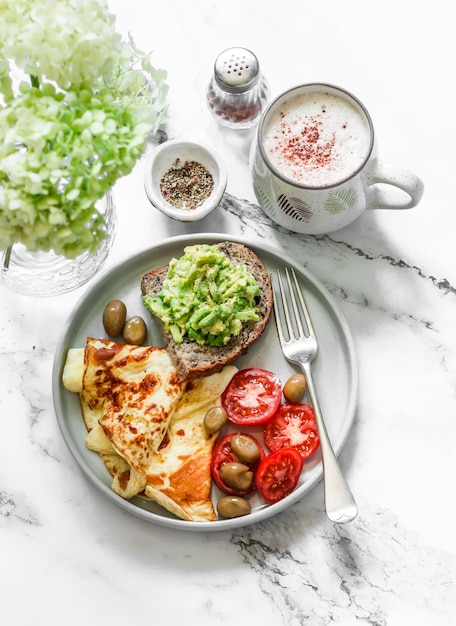 Acogedora y acogedora mesa de desayuno, tortilla, verduras, tostadas de aguacate y capuchino sobre un fondo de mármol claro, vista superior