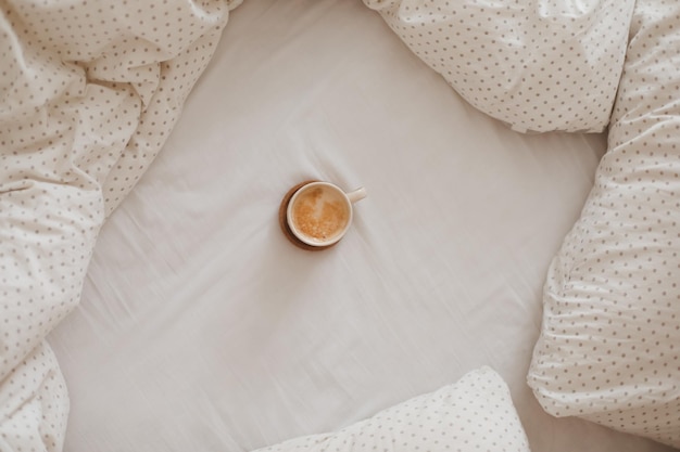 Acogedora cama desordenada sin hacer con una taza de café en el desayuno de la mañana en la cama