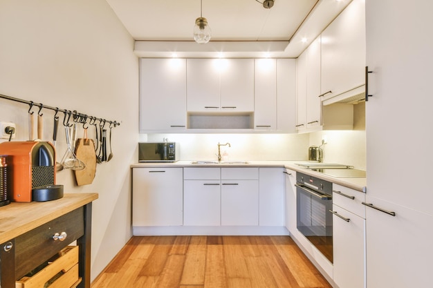 Acogedora cocina minimalista con muchos gabinetes en blanco y electrodomésticos modernos en un apartamento acogedor
