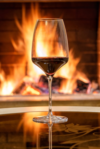 Acogedora escena de chimenea y copa de vino tinto, reflejo de un fuego en una mesa de cristal.