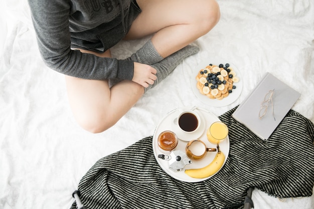 Acogedora escena de desayuno en la cama en un fin de semana con café y gofres