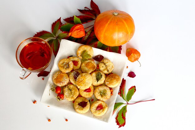 Acogedora escena de humor otoñal con hojas secas. Galletas caseras con té, hojas de otoño y calabaza