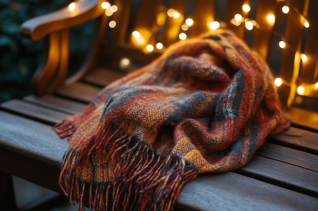 Una acogedora manta naranja y roja drapeada sobre un banco de madera rodeada de cálidas luces parpadeantes en un entorno pacífico al aire libre