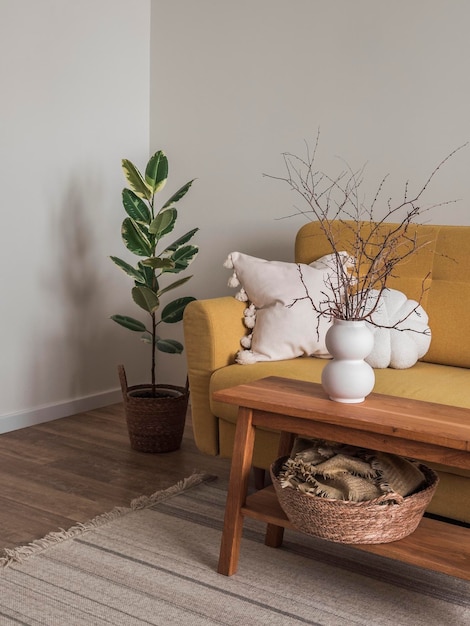 Acogedora sala de estar un banco de madera con ramas secas en un jarrón de cerámica cerca de un sofá amarillo con almohadas decorativas