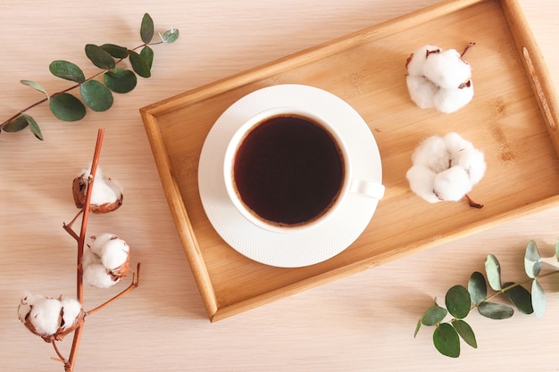 Acogedora taza de café plana casera con hojas de eucalipto y flores de algodón