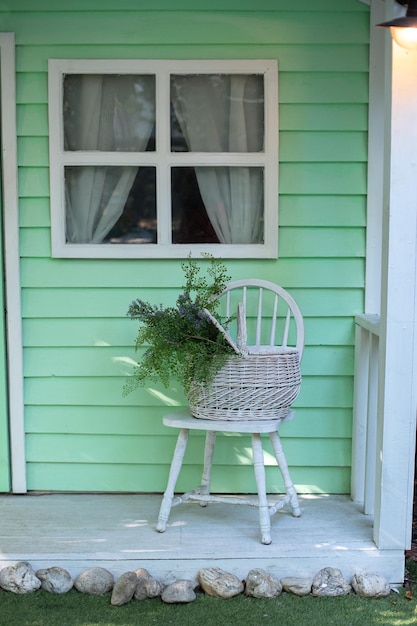 Acogedora terraza decorada con silla y cesta con flores en verano en el porche delantero para relajarse