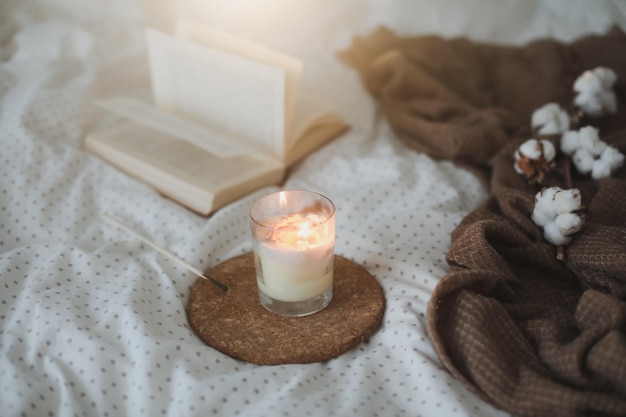 Acogedores detalles interiores de bodegones con una vela de libro y una flor de algodón en una cama cálida y suave